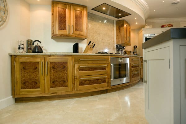 Kitchen with burr elm veneers on door panels, showing a curved run of cabinets with marble worktops and integrated oven and hob