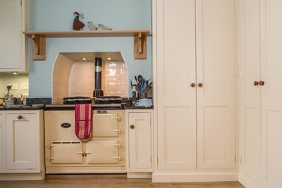 View of Aga range cooker recessed in to chimney breast with shelf above. To the right of the Aga is a large larder cupboard in the adjoining alcove