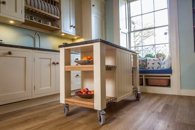 End on view of mobile kitchen island with granite worktop, shelving and lockable wheels