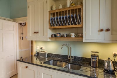 View of the sink and draining board integated in to the granite worktop with crockery storage above.