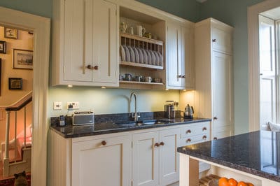 View of a run of cabinets with granite worktops integrating the sink and draining board with crockery storage  and wall mounted cupboards above.